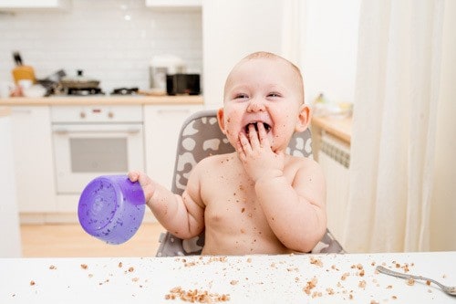 Little baby eating at kitchen. Happy messy eater
