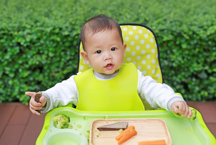 baby eating in green high chair with finger foods in front 