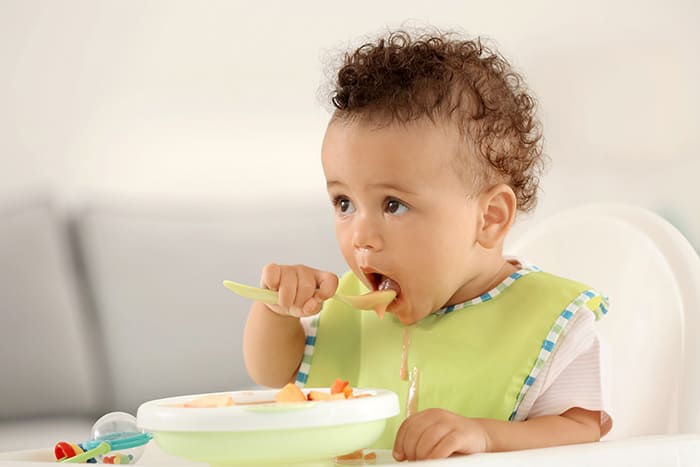 baby using spoon to eat out of a bowl
