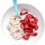 Rolled oats oatmeal with cut strawberries on white background