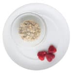 steel cut oatmeal in glass bowl with raspberries on the side