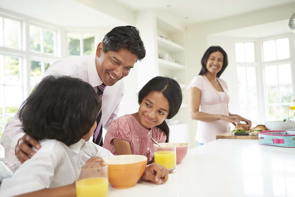 mom standing at counter watching kids talking to dad and eating